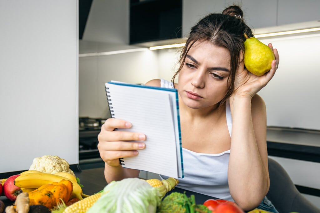 uma jovem na cozinha com um notebook entre legumes