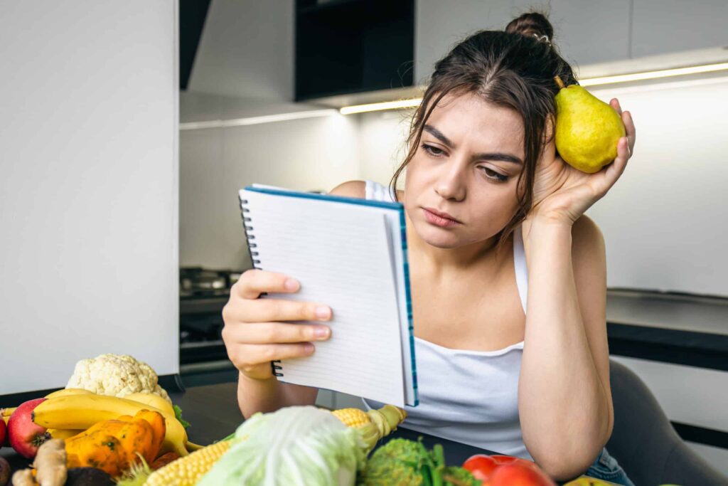 uma jovem na cozinha com um notebook entre legumes scaled 1