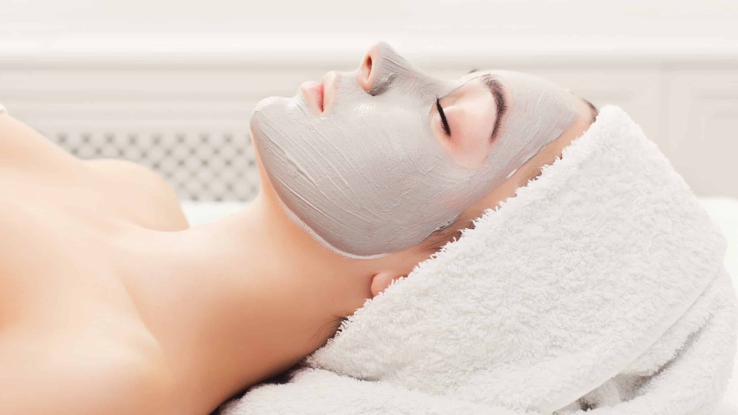 Máscaras Faciais Nutritivas e Calmantes 5 Face mask, spa beauty treatment. Woman applying facial clay mask at spa salon, skincare, top view, overhead