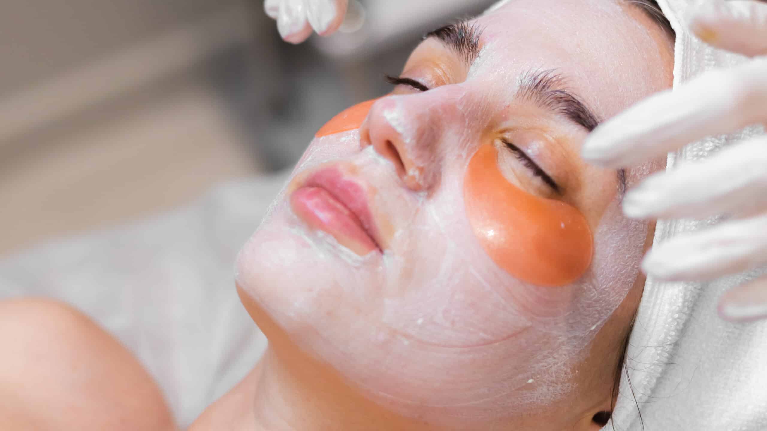 Máscaras Faciais Nutritivas e Calmantes 9 A young girl in a beauty salon in a cosmetology room lies on a bed relaxes with a mask on her face and patches under her eyes